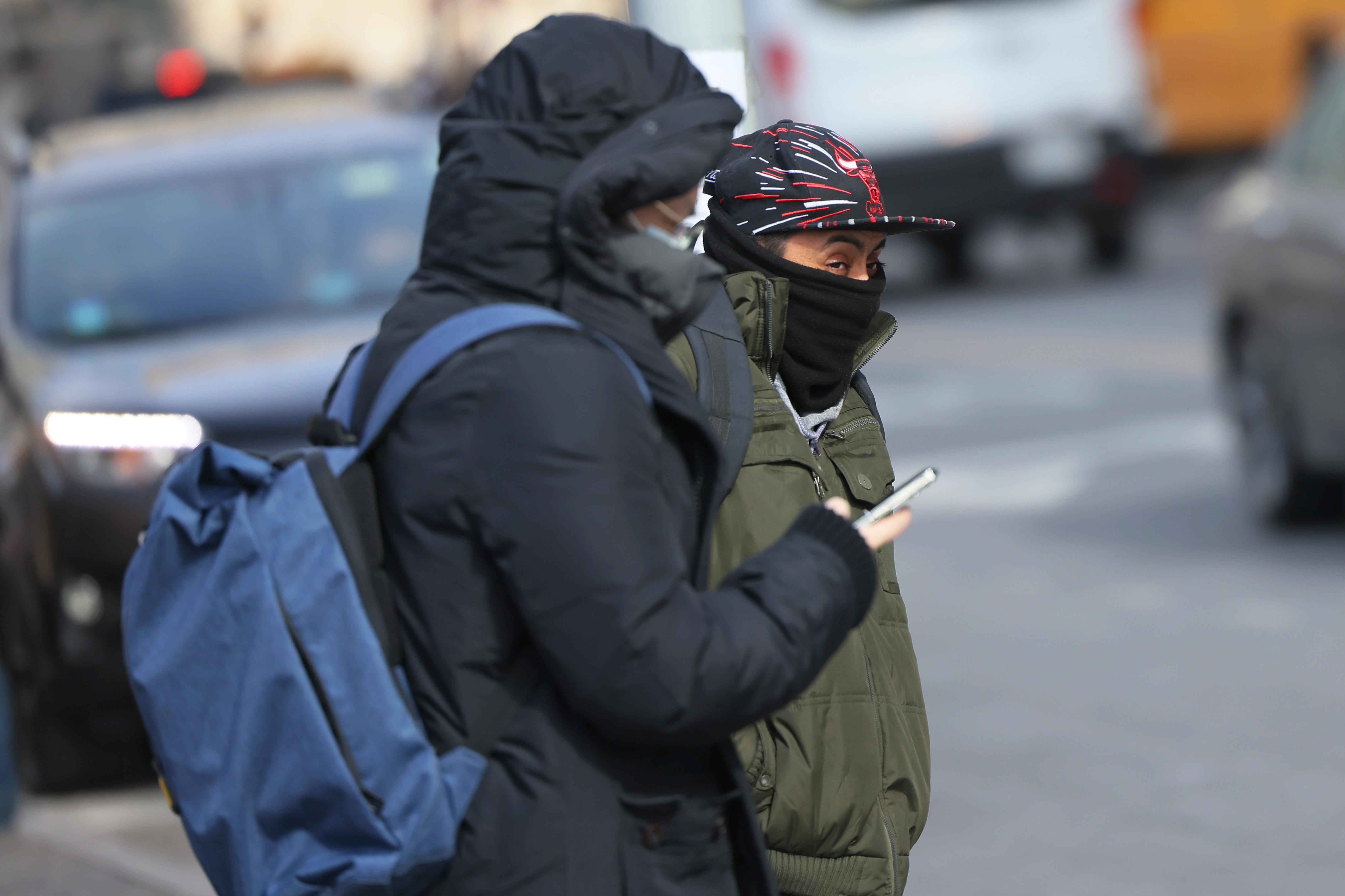 Two people stand outside in New York City bundled up in coats.