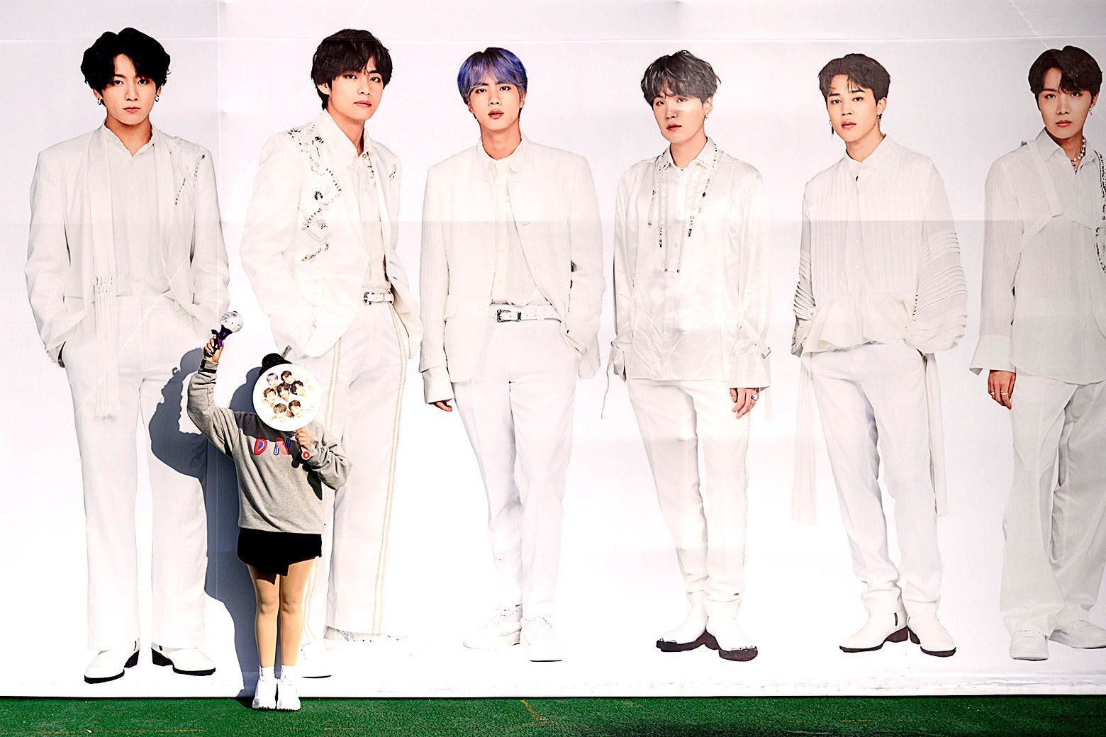 A fan poses for photos in front of a large image of BTS