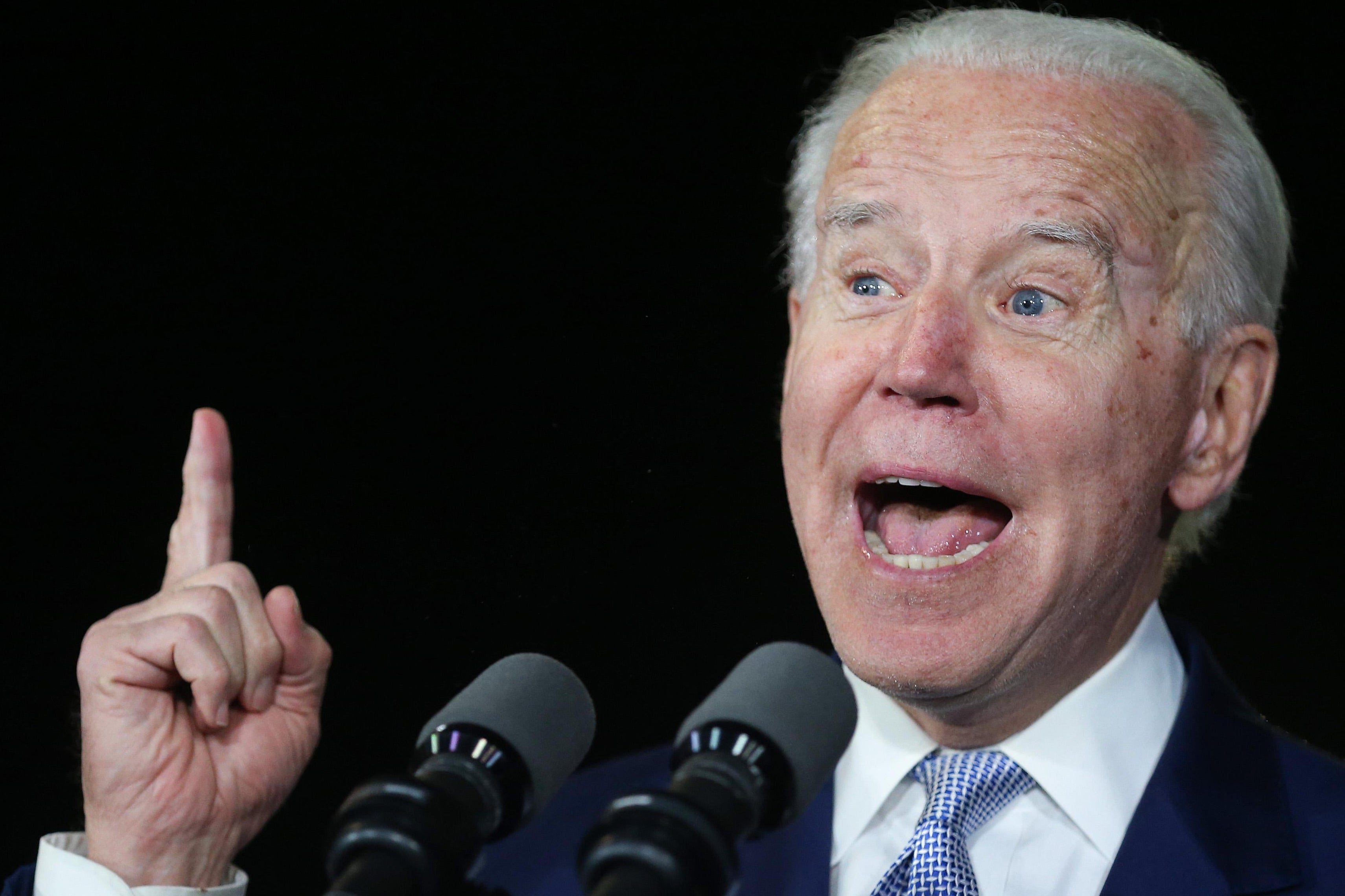 Joe Biden stands in front of a microphone with mouth agape.