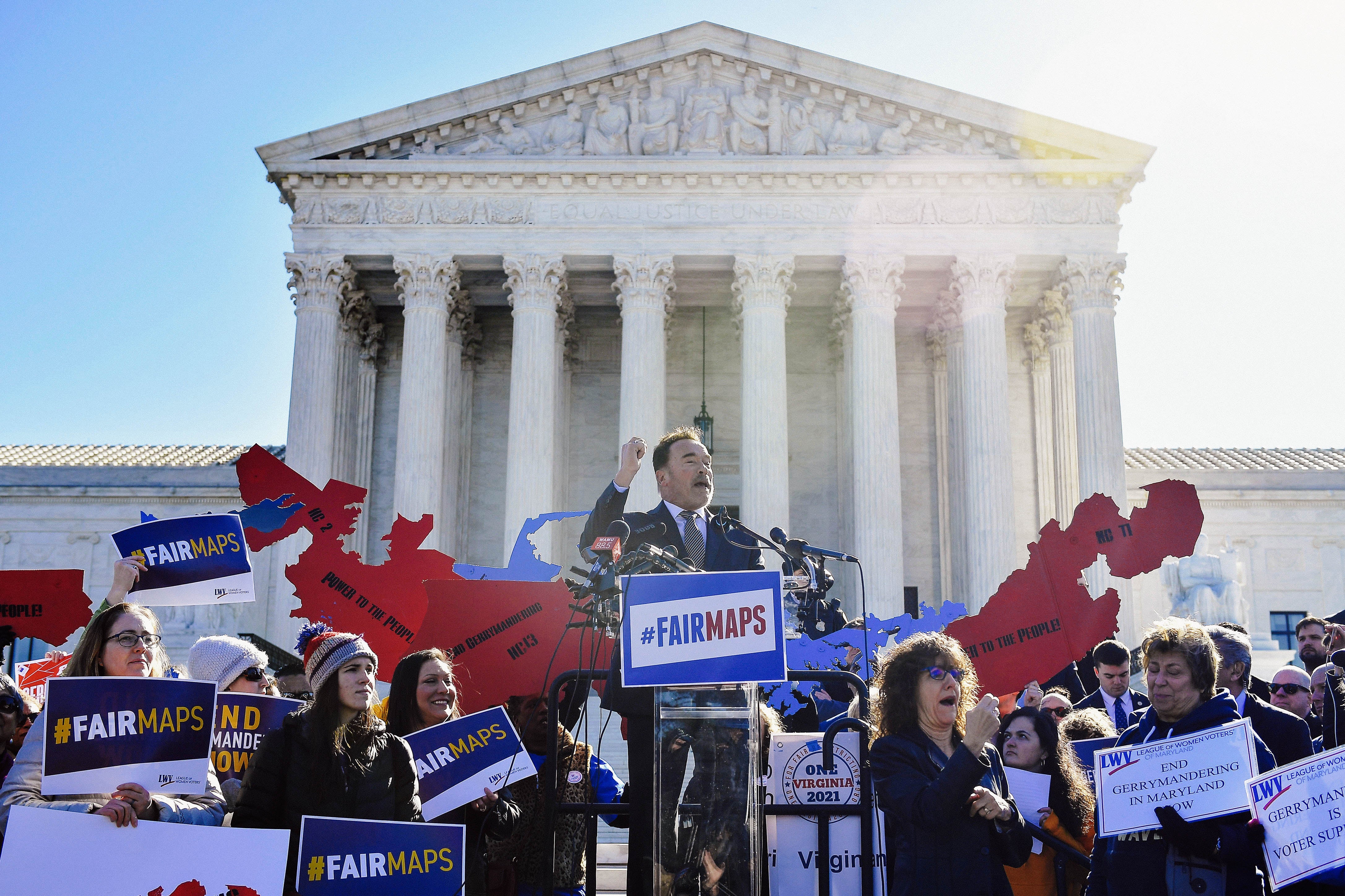 Schwarzenegger speaks at a podium in front of the Supreme Court building with a crowd around him.