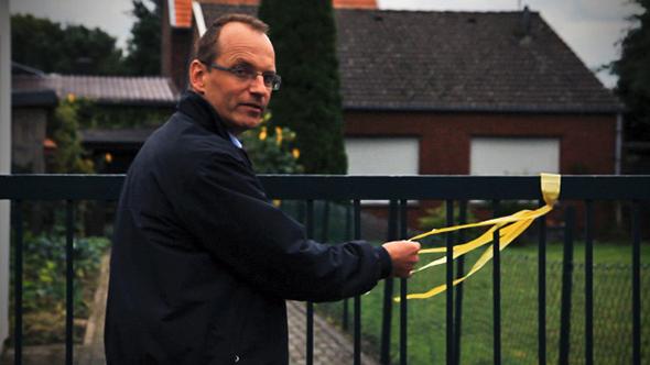 Dirk Jansen ties a yellow ribbon around a fence.