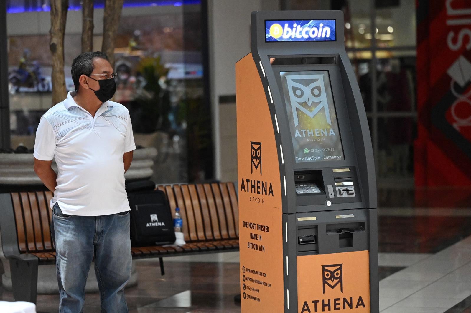 A man stands next to a Bitcoin ATM at a shopping mall in San Salvador. 