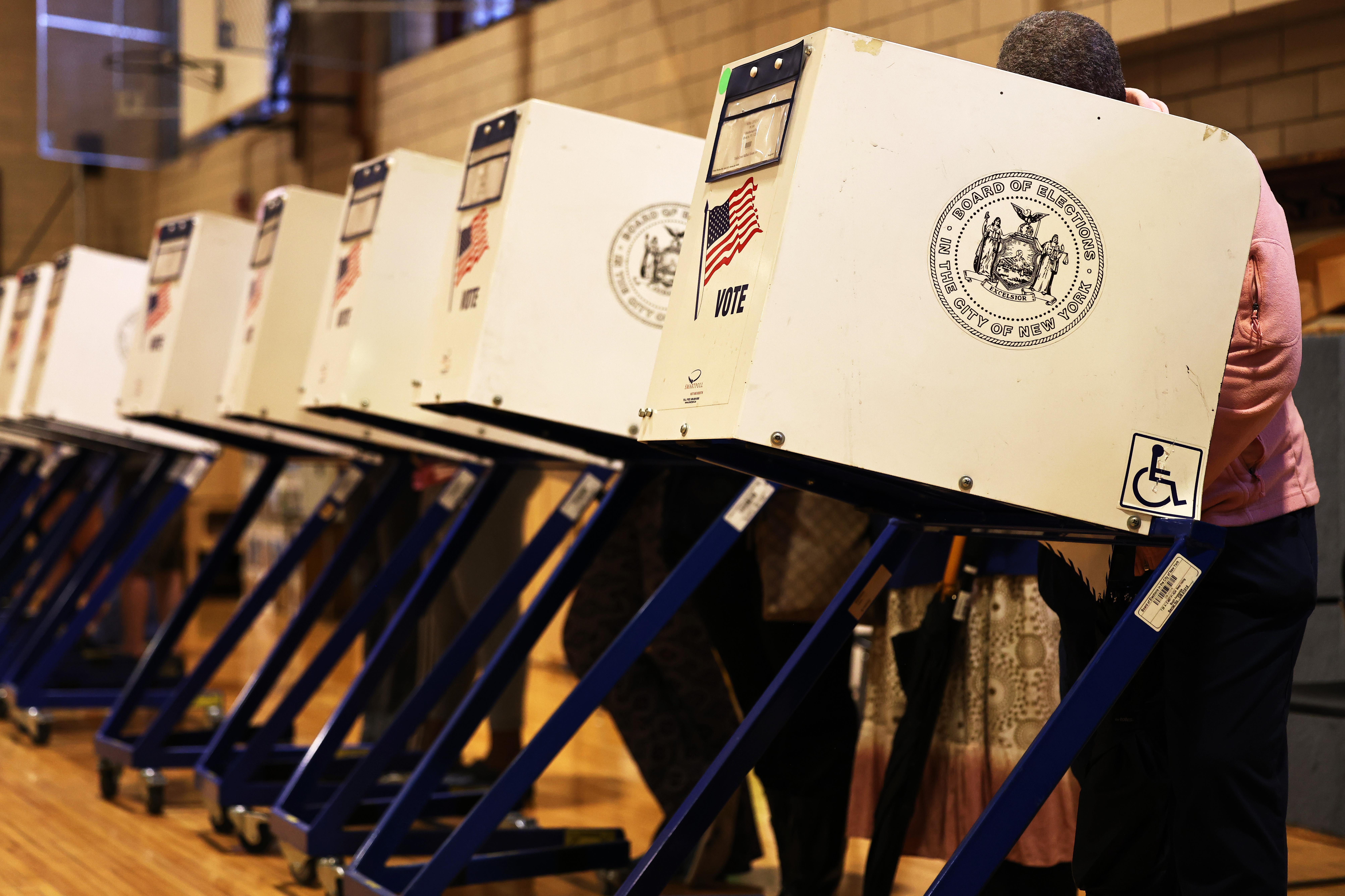 A row of people voting in voting booths indoors