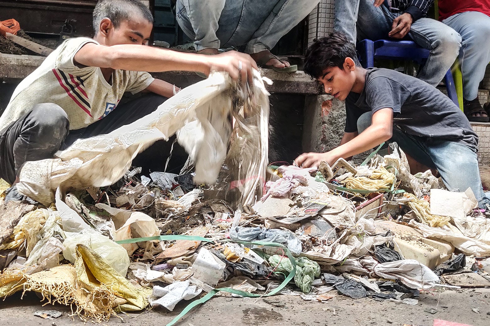 Two children sort through large white plastic bags, searching for valuable e-waste scraps. 