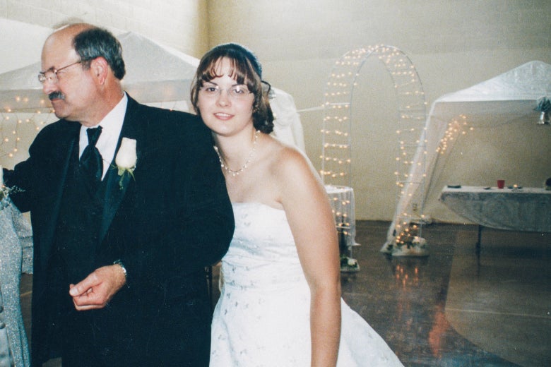 A woman in a wedding dress poses for a photo next to her father.