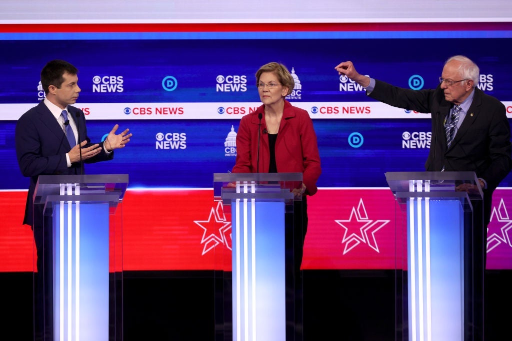 Buttigieg and Sanders gesture at each other from their lecterns as Warren stands between them.