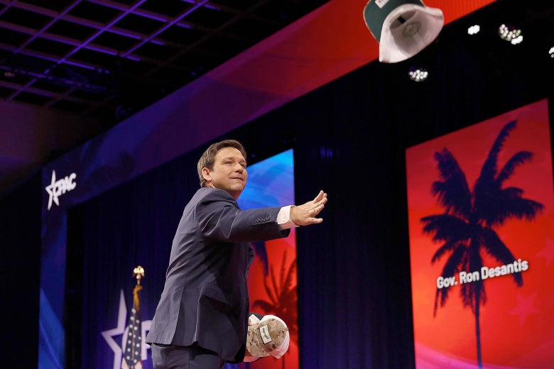 Ron DeSantis stands onstage tossing a hat to the crowd at CPAC