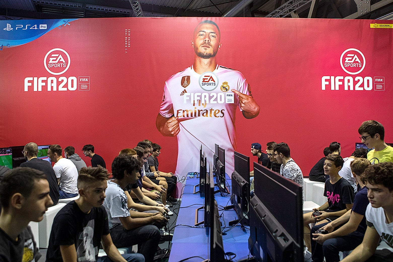 Gamers sit at rows of computers. A picture of a FIFA player along with the FIFA and EA logos is seen over them.