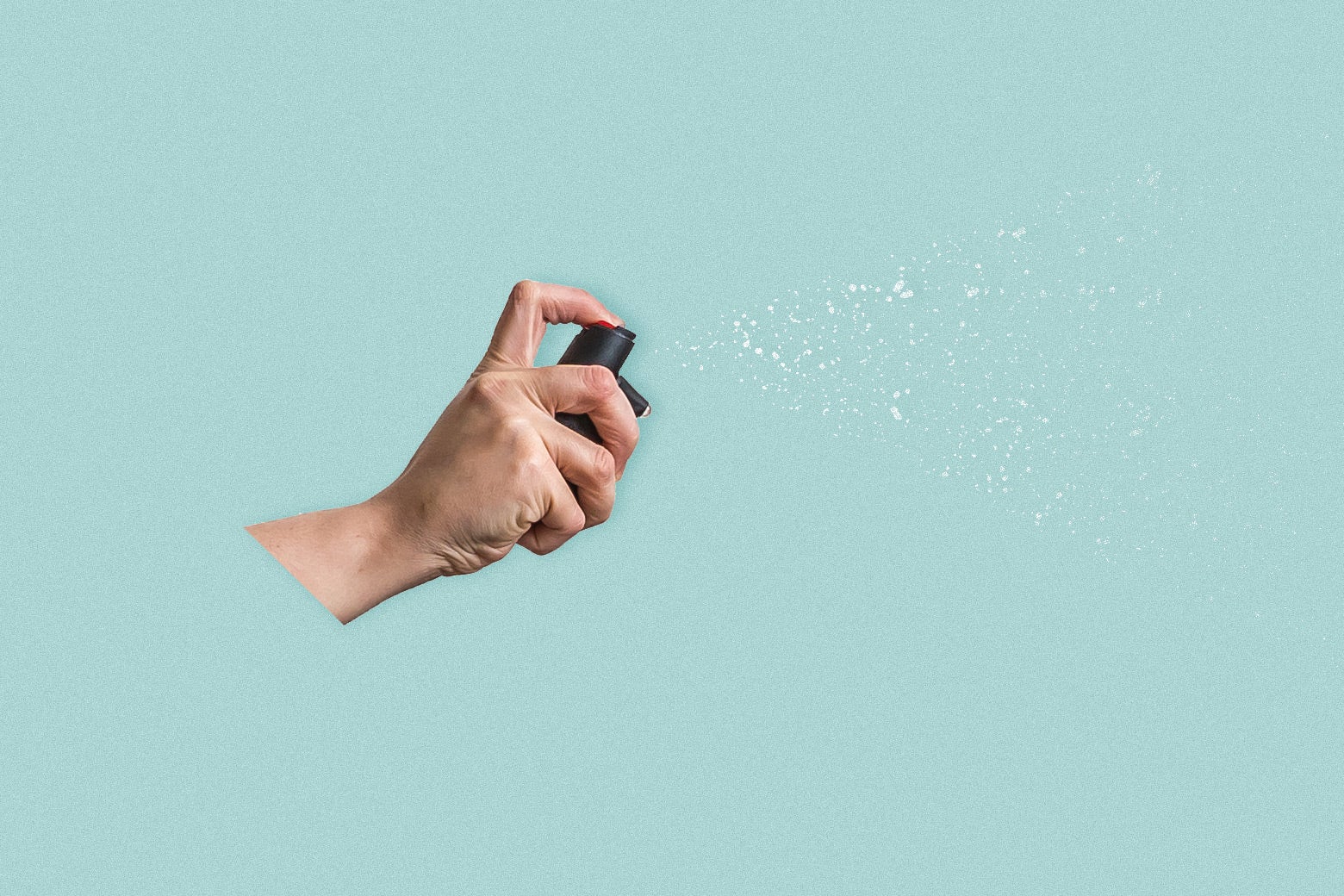 A hand holding pepper spray against a blue backdrop. 