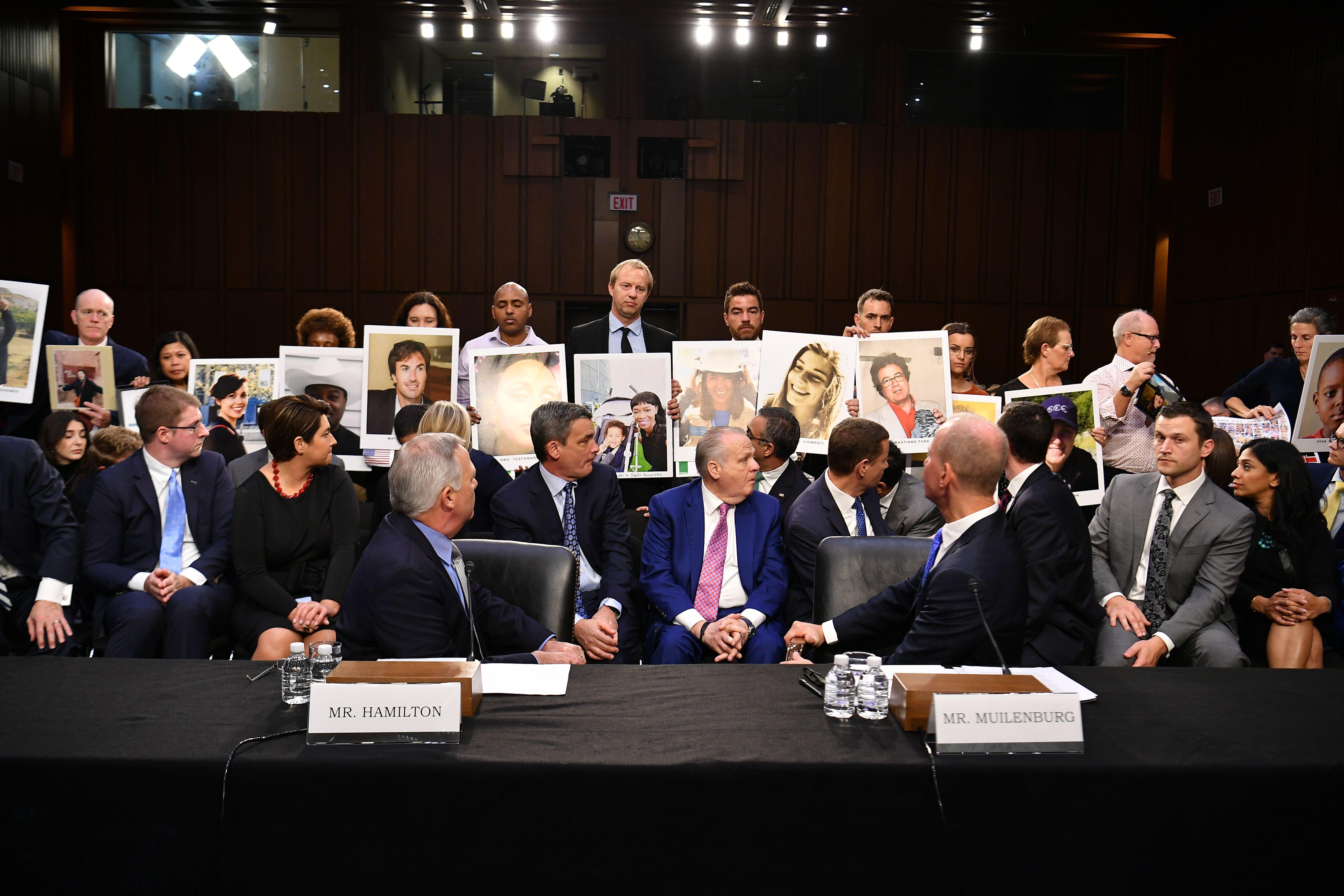 Boeing executives and other attendees of the committee hearing turn to face family members who hold up photos of Boeing 737 Max crash victims