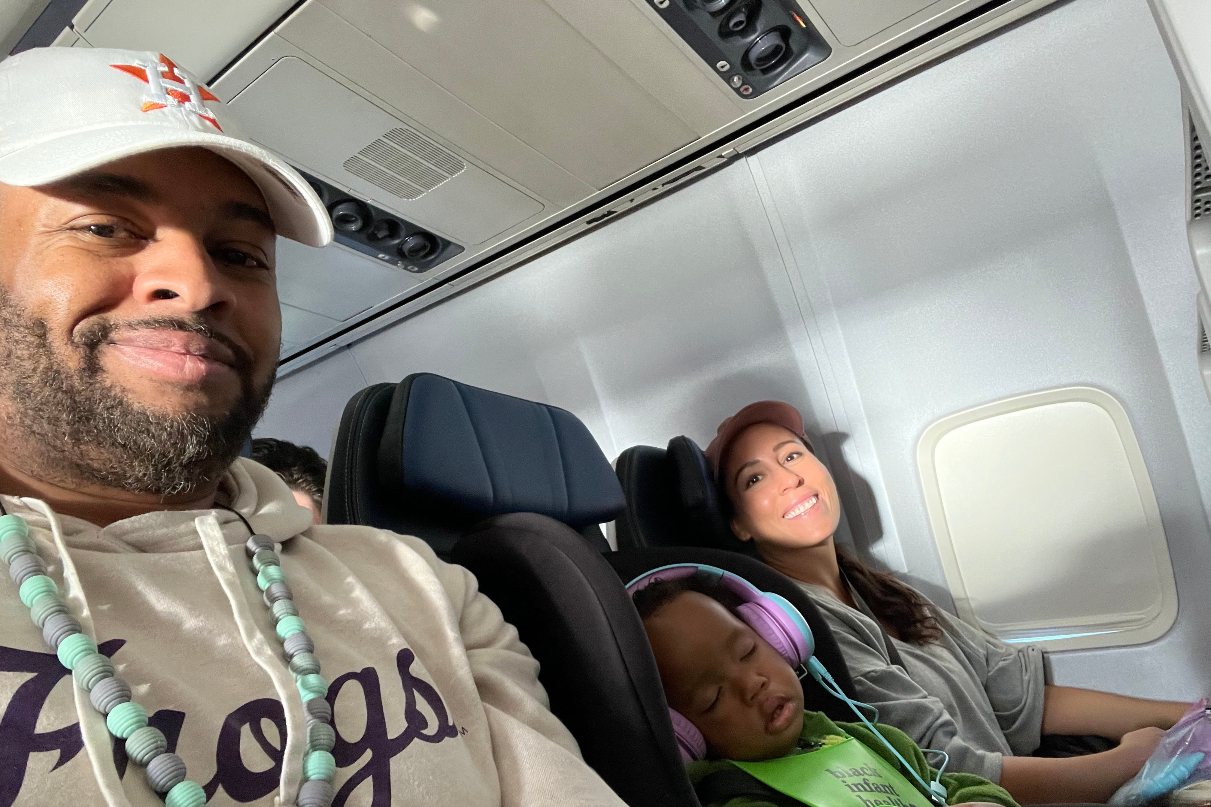 A sleeping baby in between two happy parents on a plane.