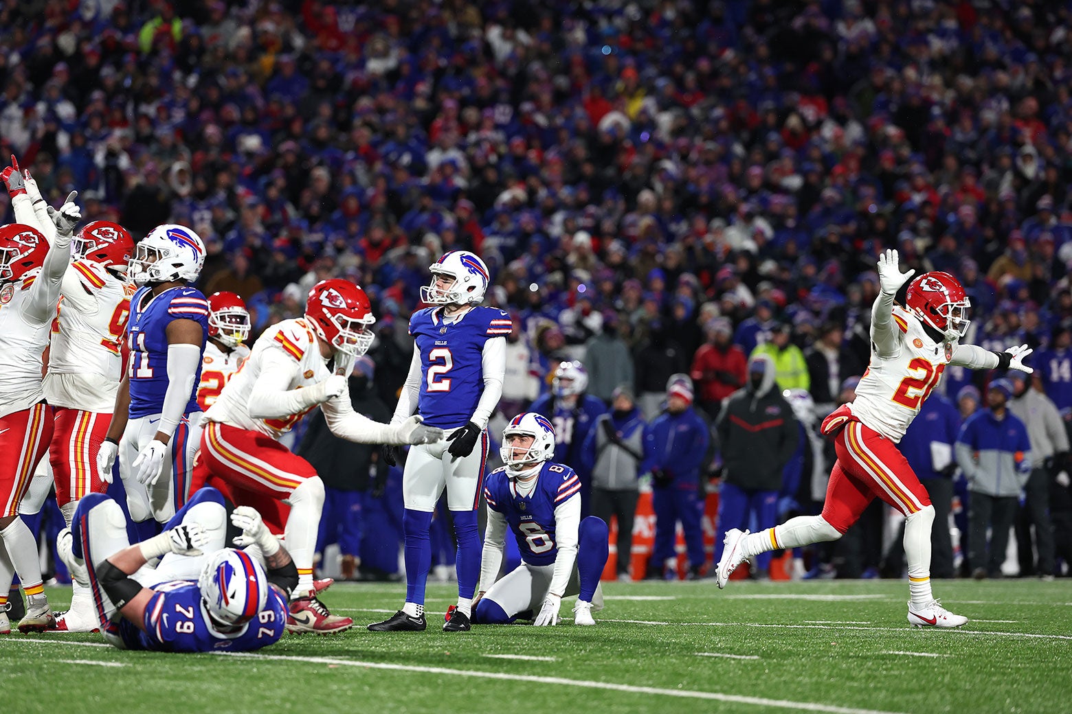 Bills kicker Tyler Bass looks at the sky in disbelief after his missed field goal, the Chiefs celebrating around him, one player running with his arms spread out wide like he is flying.