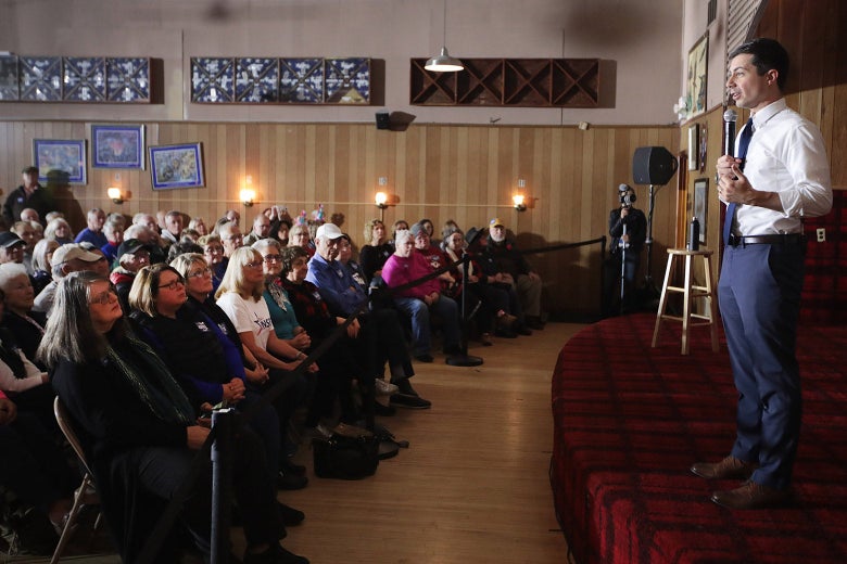 Buttigieg speaks into a mic onstage in front of a seated crowd.