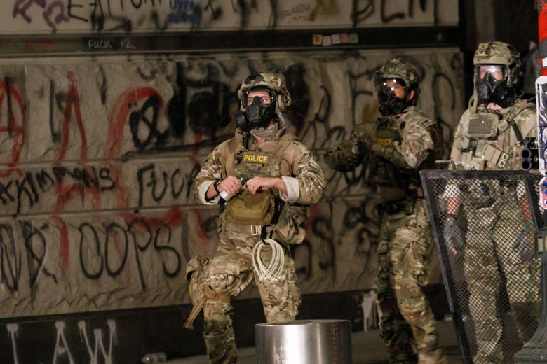 Federal agents in camouflage military gear walk down a street in Portland, Oregon.