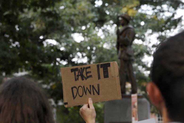 A man holds a sign that says "Take it down." Silent Sam is seen in the background.