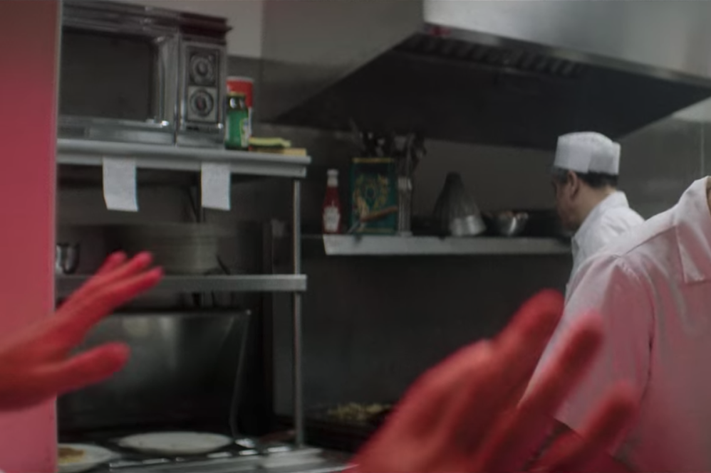 Lin-Manuel Miranda, can be seen through a diner kitchen window dressed as a line cook looking down.