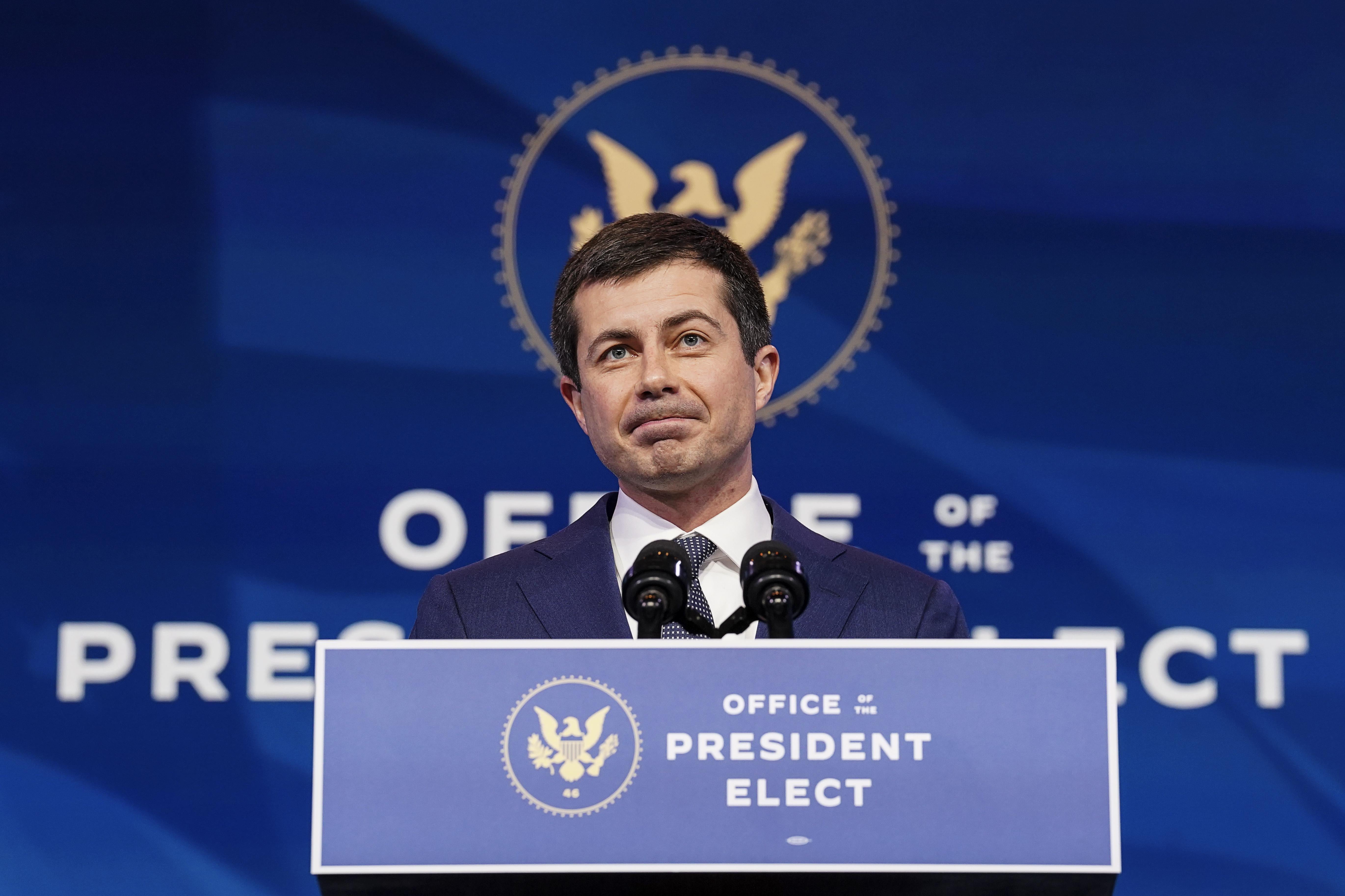 Pete Buttigieg stands onstage at a podium marked Office of the President Elect