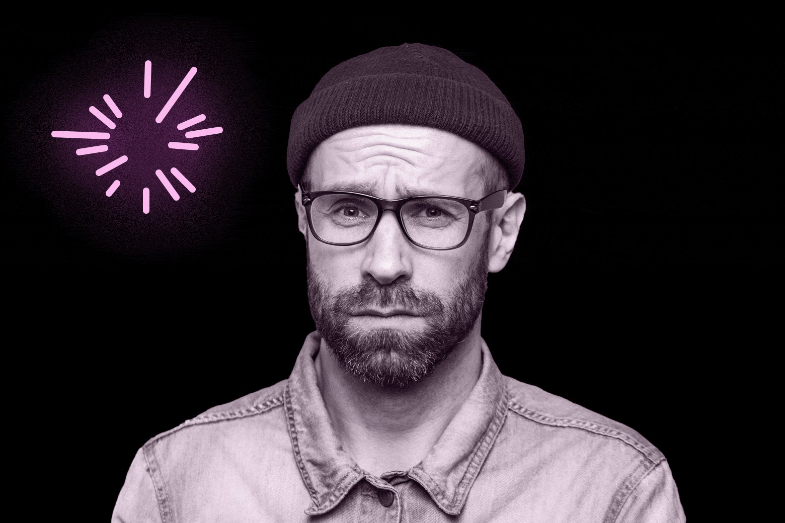 Man in a beanie and glasses staring at the camera with fireworks going off around him.