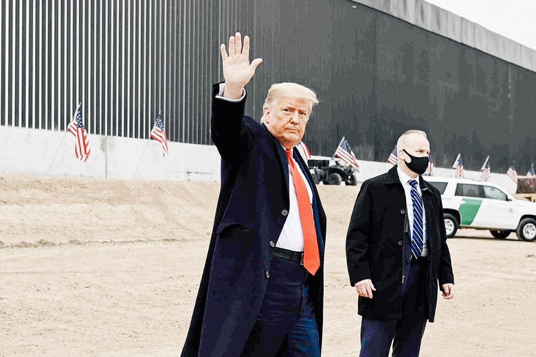 Trump waves will standing near the border wall.