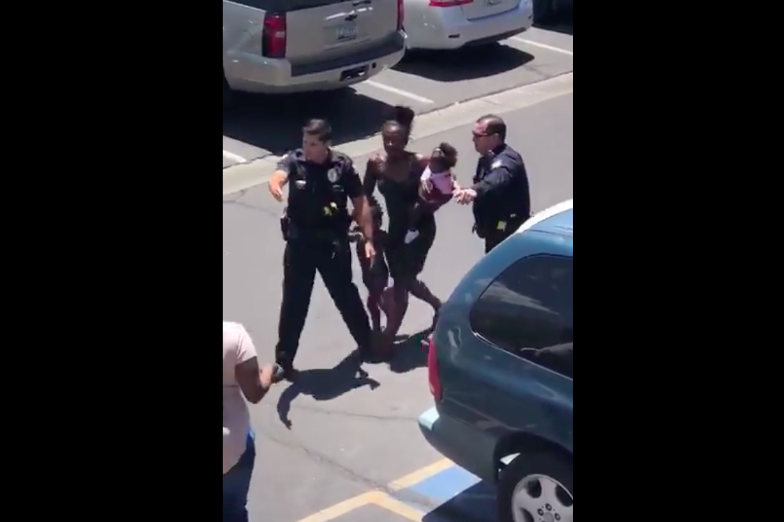 Iesha Harper is seen carrying a child in one arm and holding another child by the hand, surrounded by two police officers.
