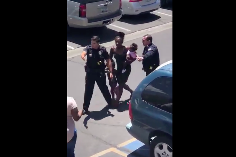 Iesha Harper is seen carrying a child in one arm and holding another child by the hand, surrounded by two police officers.