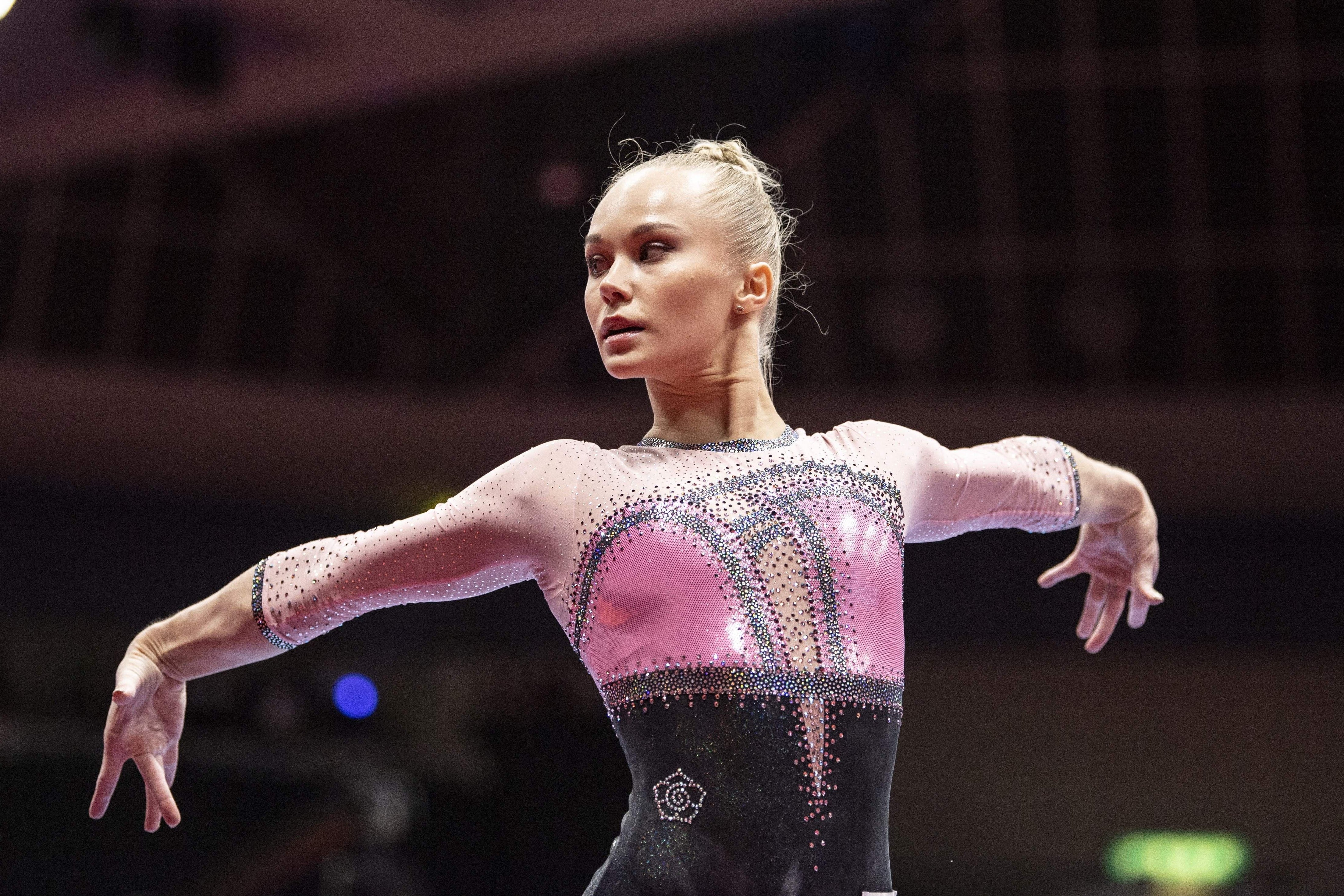 Melnikova in her leotard with her arms splayed outward and behind her, her head turned to her right