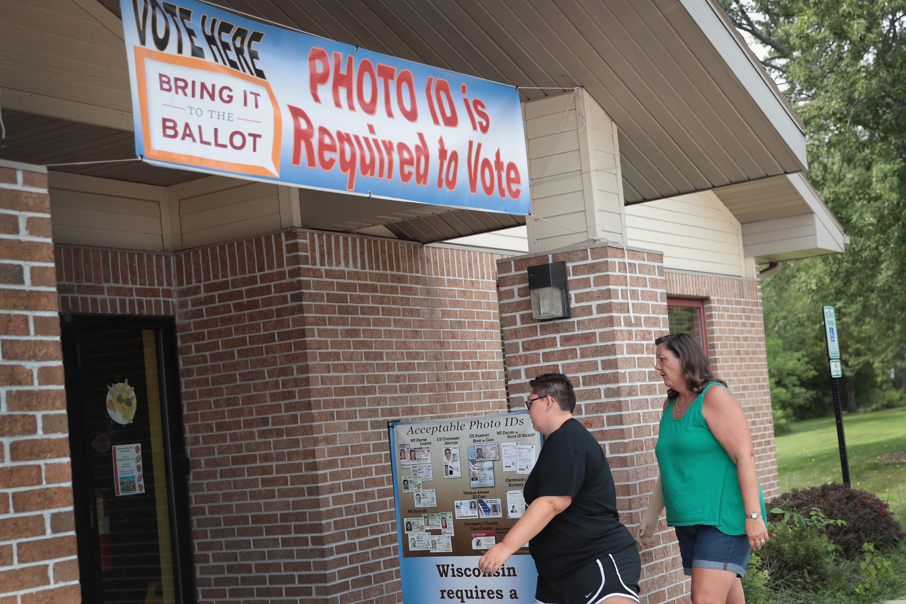 Two people walk into a polling place that has a sign out front warning voters that photo ID is required to vote.