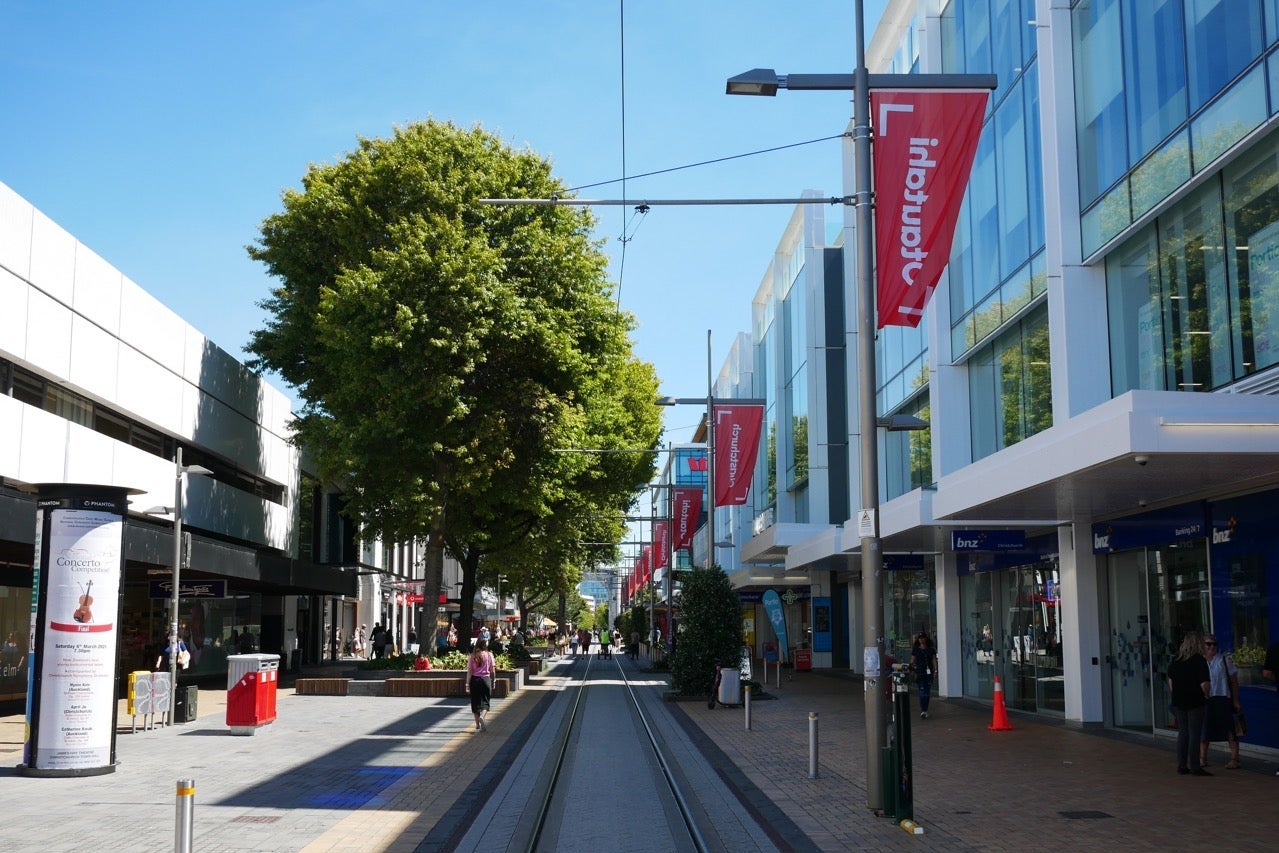 A few shoppers walk down a pedestrianized outdoor mall.