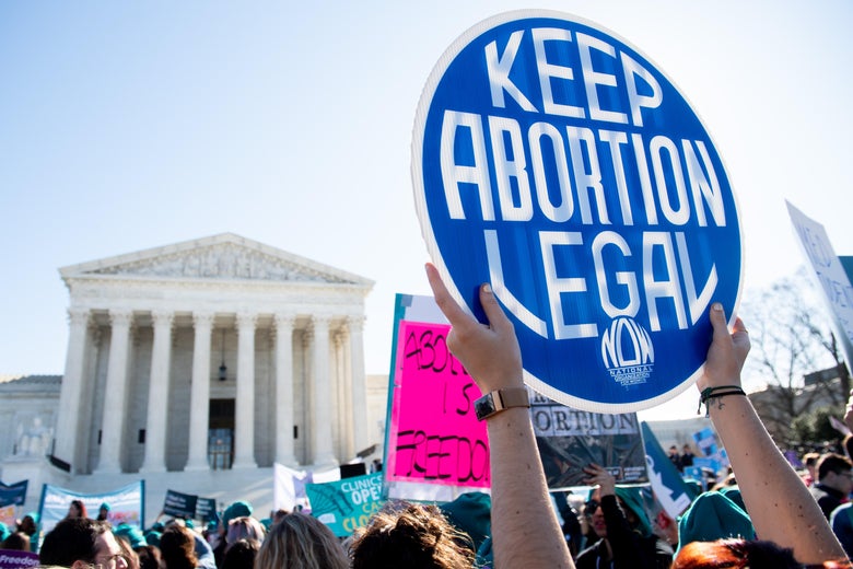 White arms hold up a "Keep abortion legal" sign in front of the Supreme Court building, amid a crowd of other protesters.