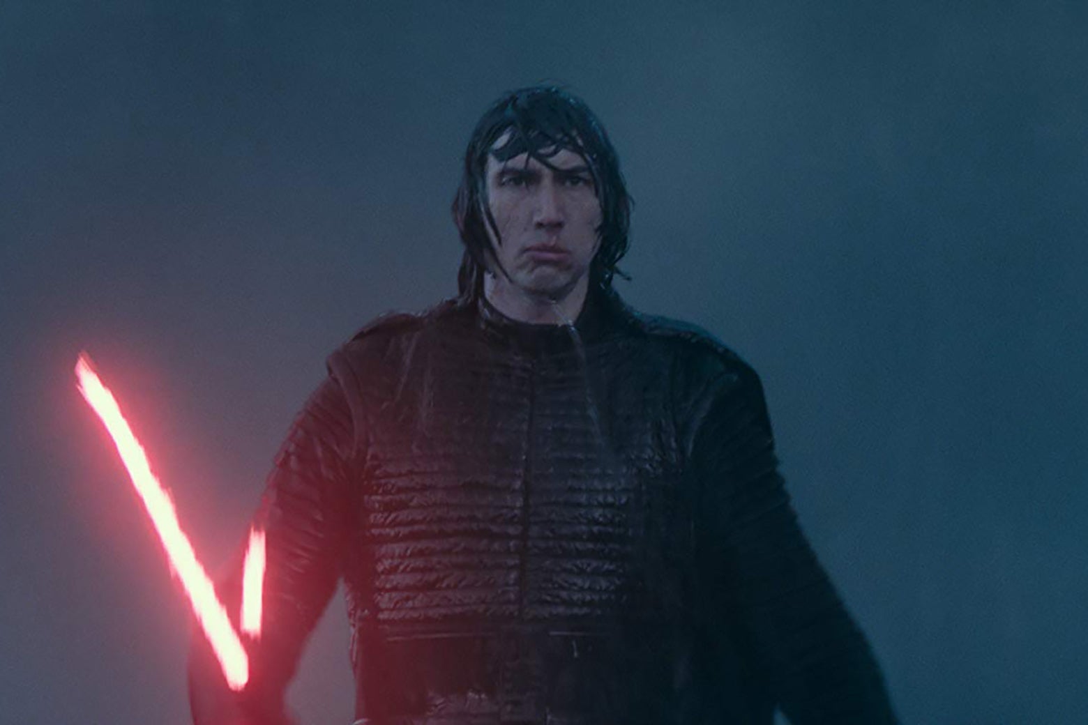 Adam Driver, in a still from The Rise of Skywalker, wearing a black leather suit and coat and wielding his red lightsaber. He looks disappointed.