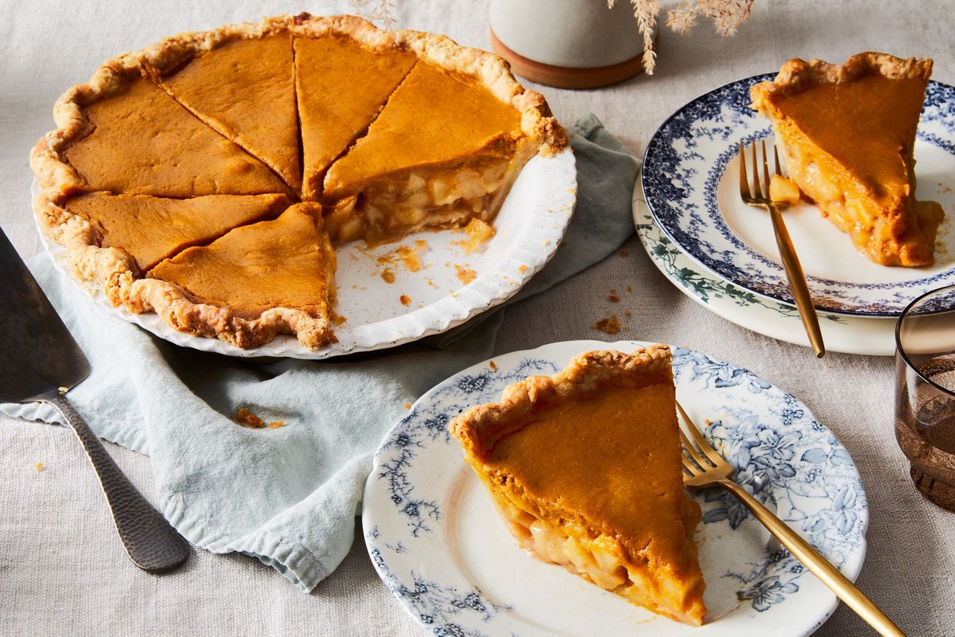 Apple cider pumpkin pie in a ceramic dish with two pie slices on plates beside it, on a tablecloth