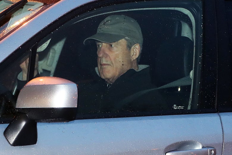 Mueller, wearing a baseball cap and looking pensive, is pictured behind the driver's side window of a car.