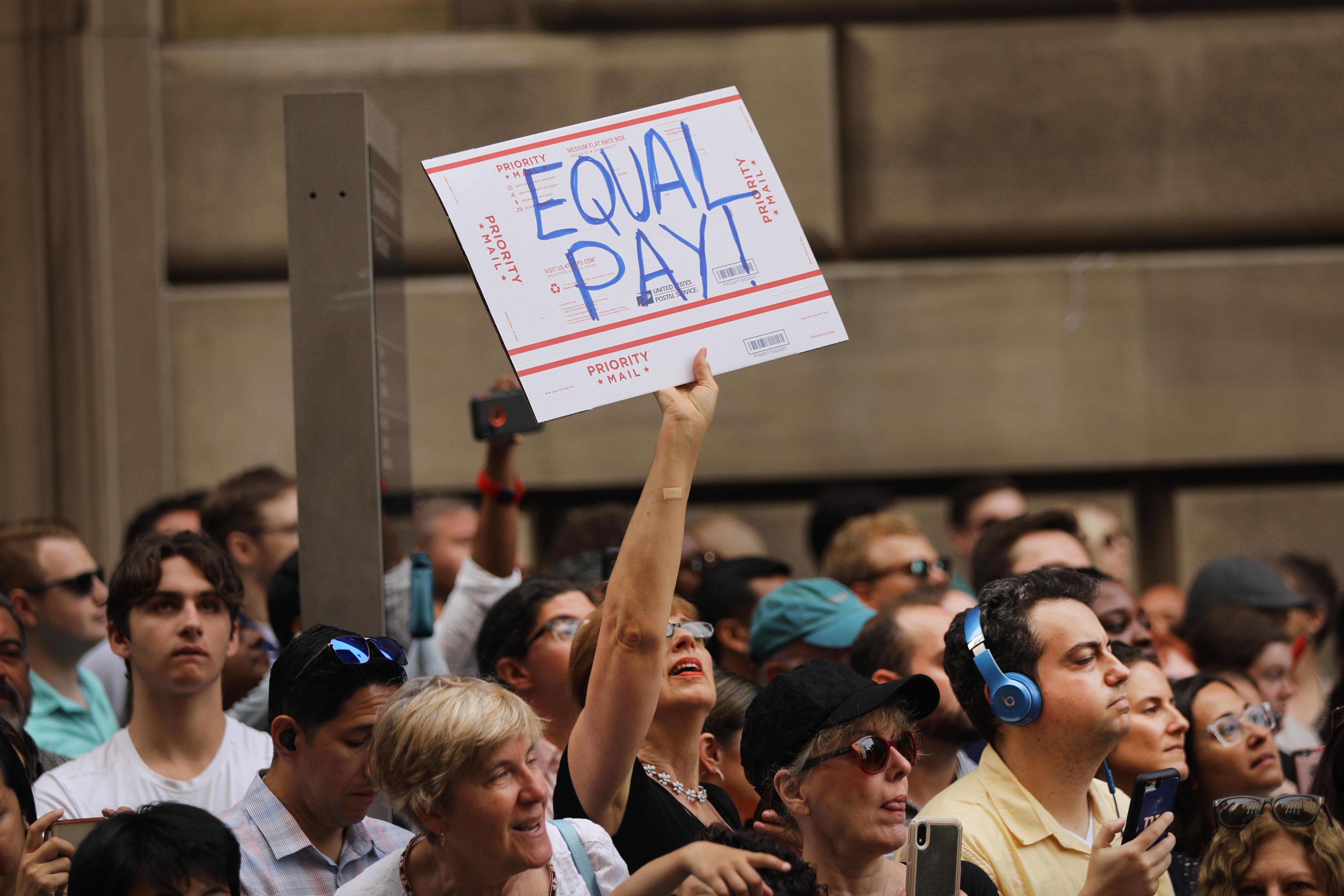 A woman holds a sign that says "Equal Pay" in a crowd of USWNT supporters.