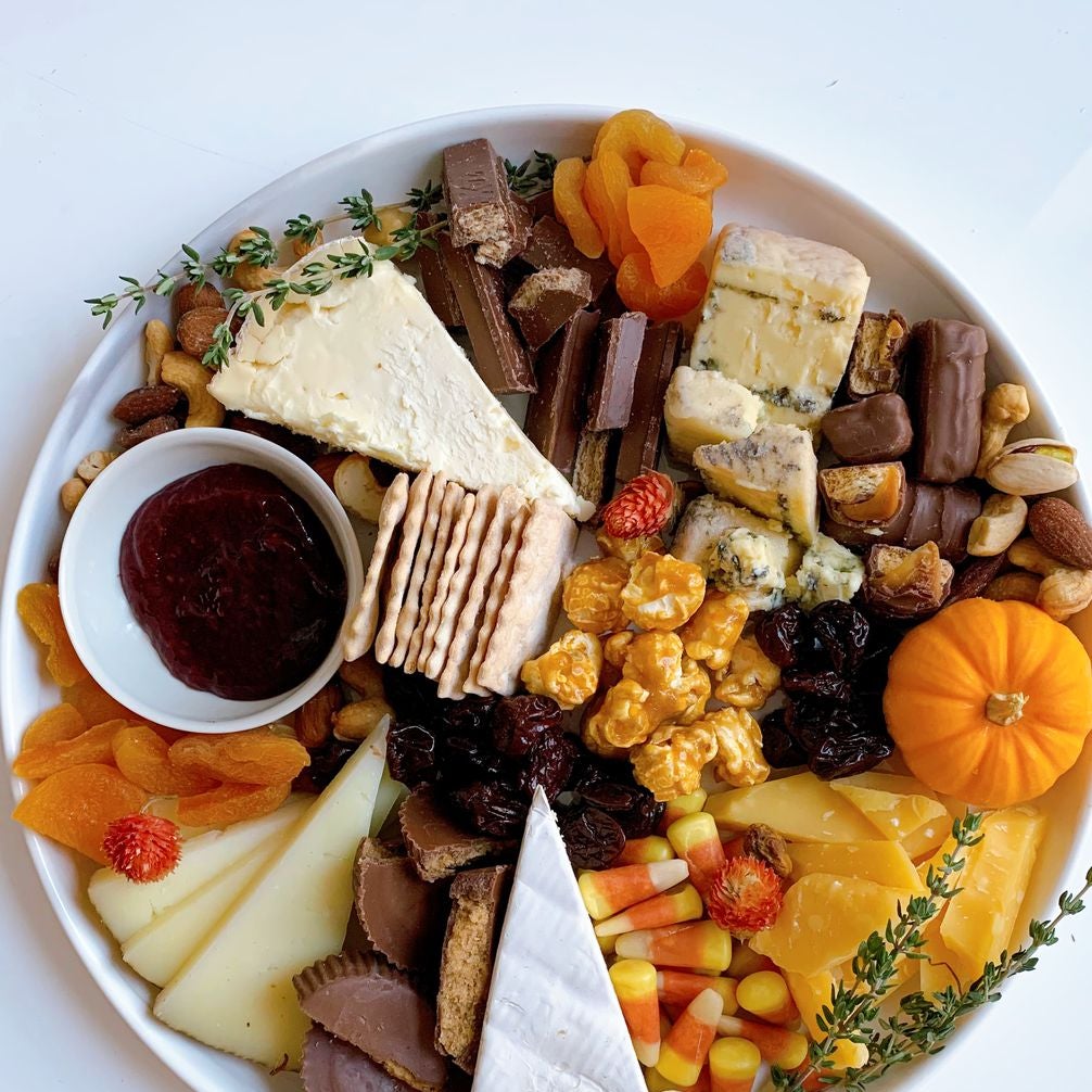 Platter of candy corn, dried fruit, caramel corn, nuts, Twix, Kit Kats, Reese's Peanut Butter Cups, crackers, and fancy cheese wedges
