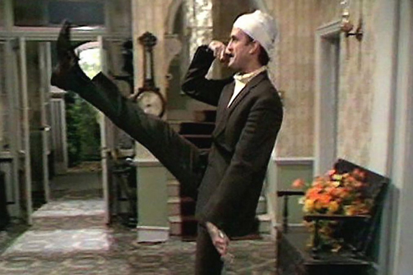 John Cleese does a goose step and holds his finger above his mouth in a makeshift Hitler mustache.