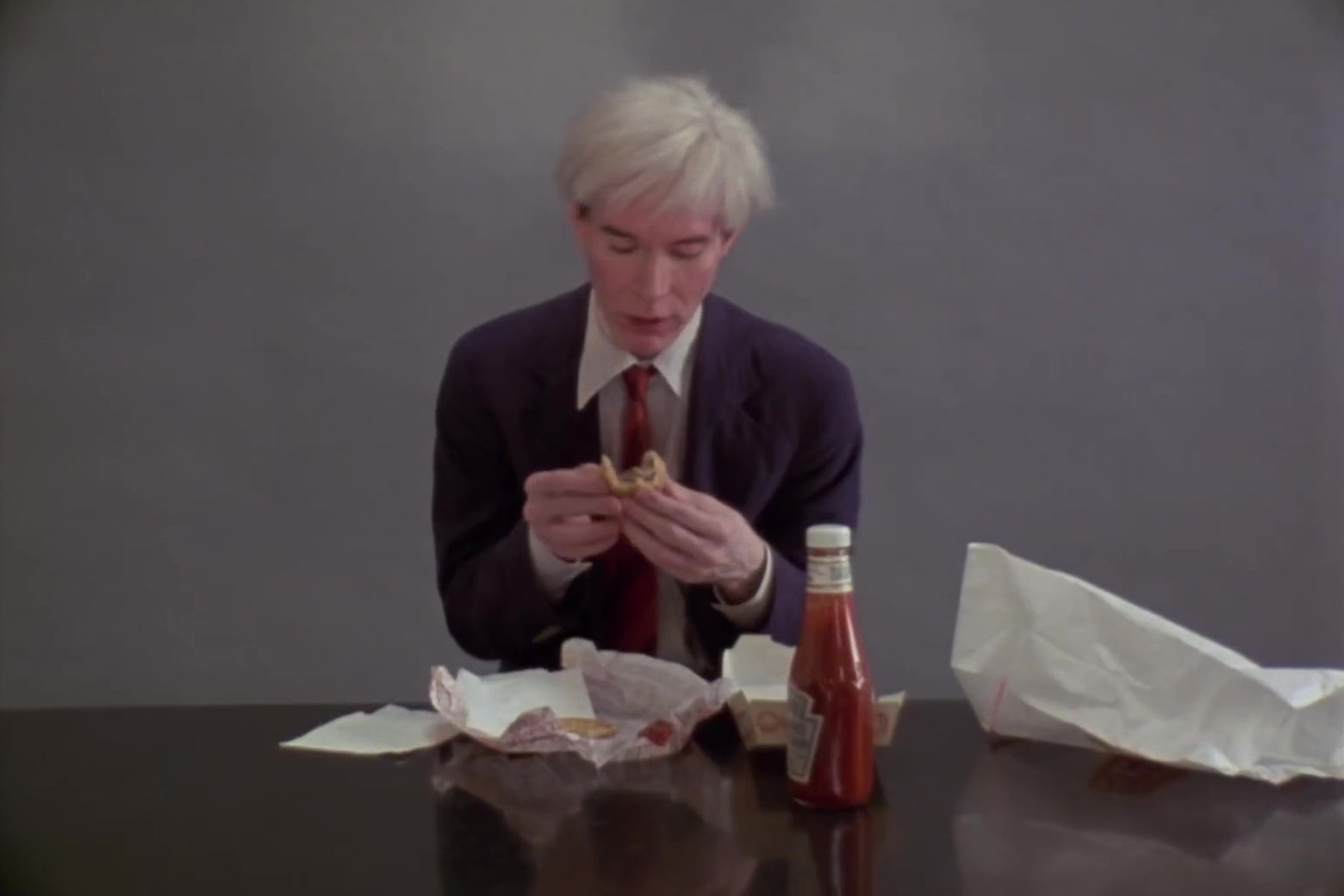 Andy Warhol, folding a Burger King hamburger in half.