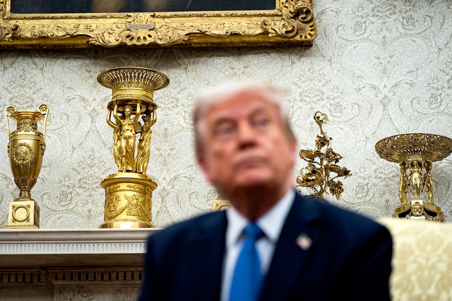 Trump in front of gold picture frames, gold statues, and gold filigrees in the Oval Office.
