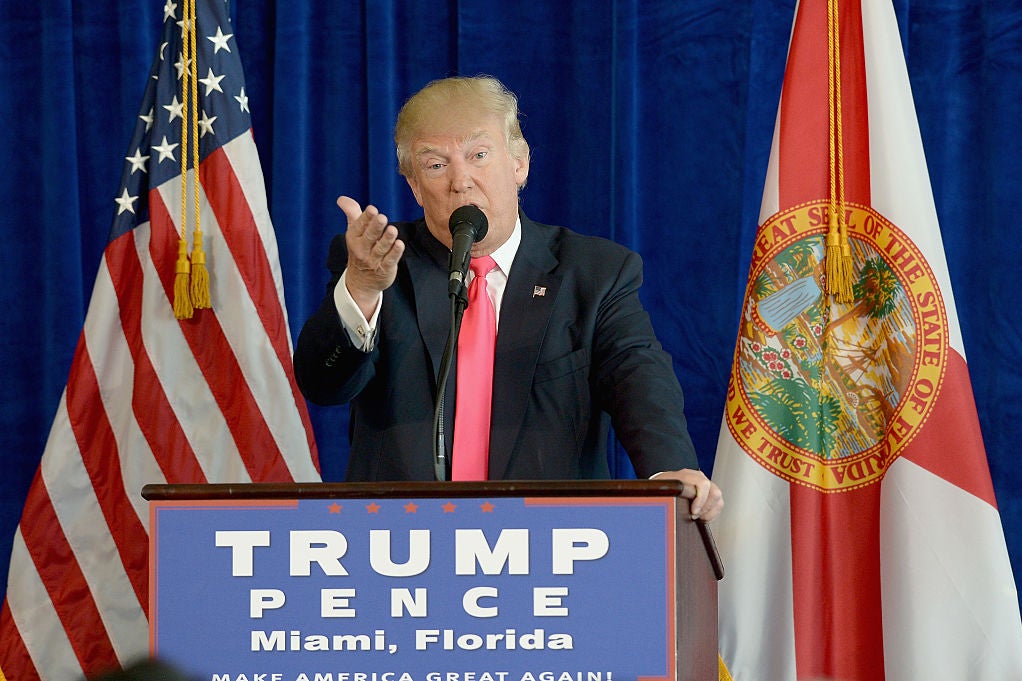 Trump gestures toward the camera while speaking against a blue backdrop.