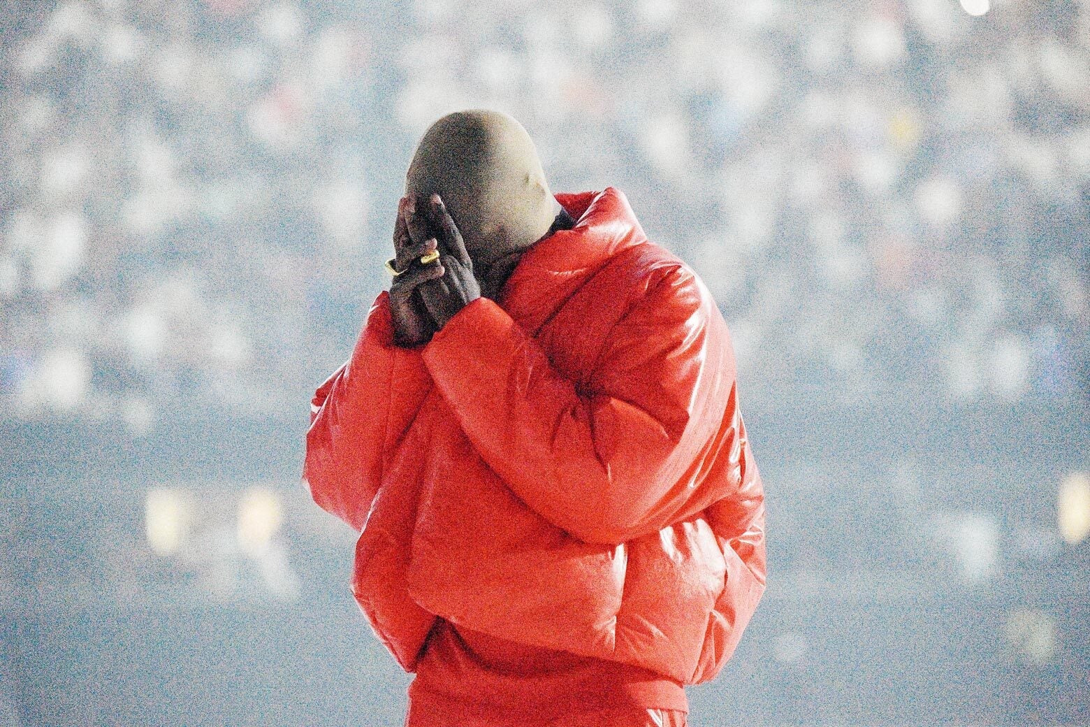 A man wearing a red puffy jacket and matching pants holds his face in his hands. 