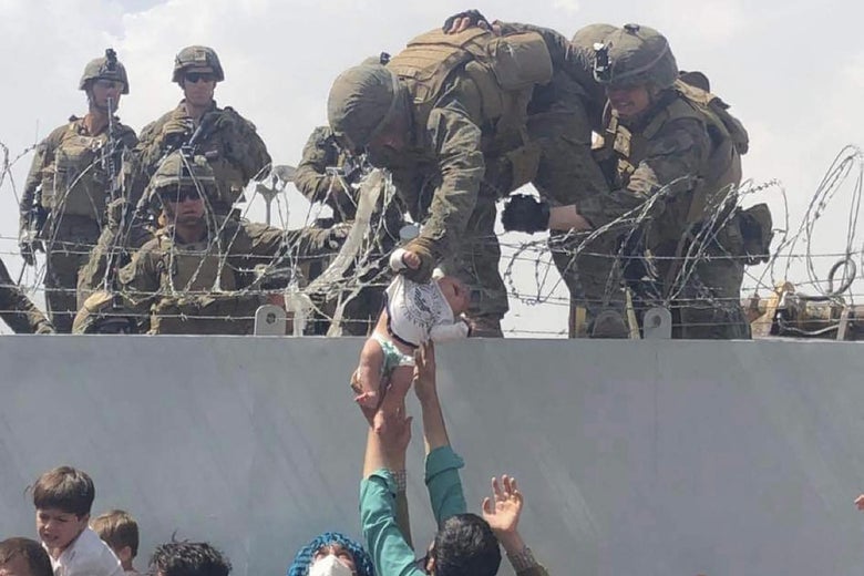 This image made available to AFP on August 20, 2021 by Omar Haidiri, shows a U.S. Marine grabbing an infant over a fence of barbed wire during an evacuation at Hamid Karzai International Airport in Kabul on August 19, 2021. 