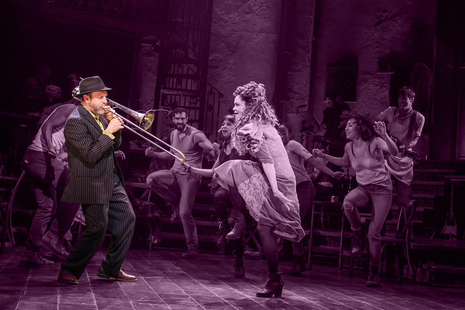 Brian Drye plays trombone with actors dancing around him onstage