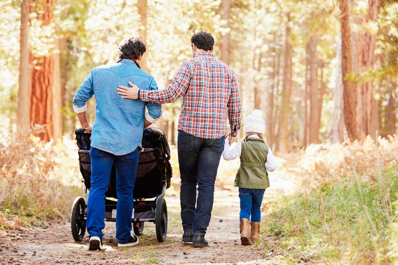 A family of two men and two children walking in the woods with a stroller.