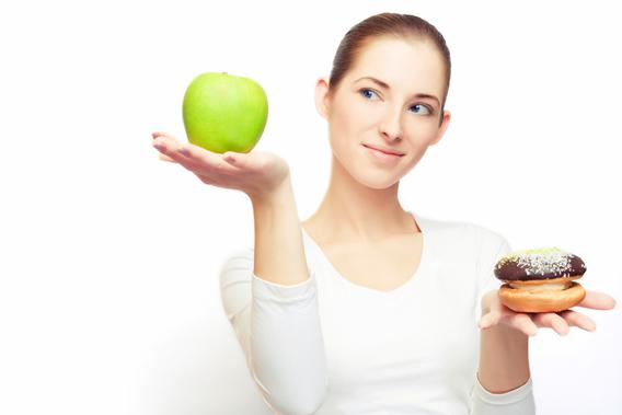 Portrait of young cheerful woman choosing between apple and cake