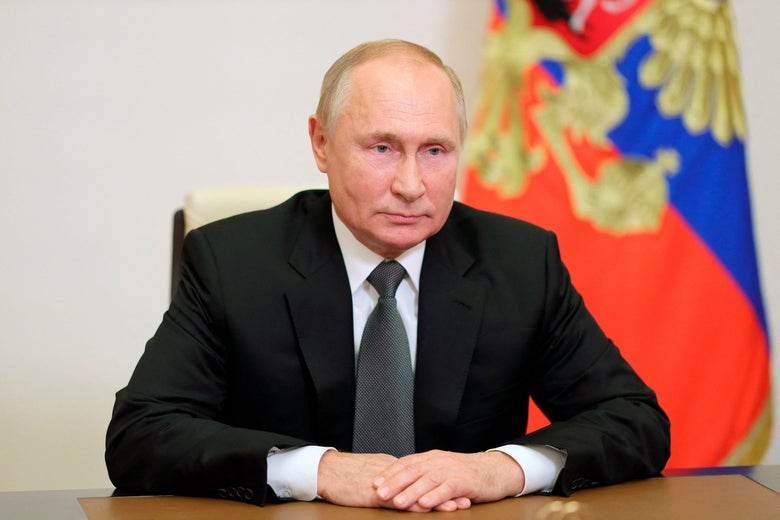 Putin sits at a table, his hands on the surface in front of him.