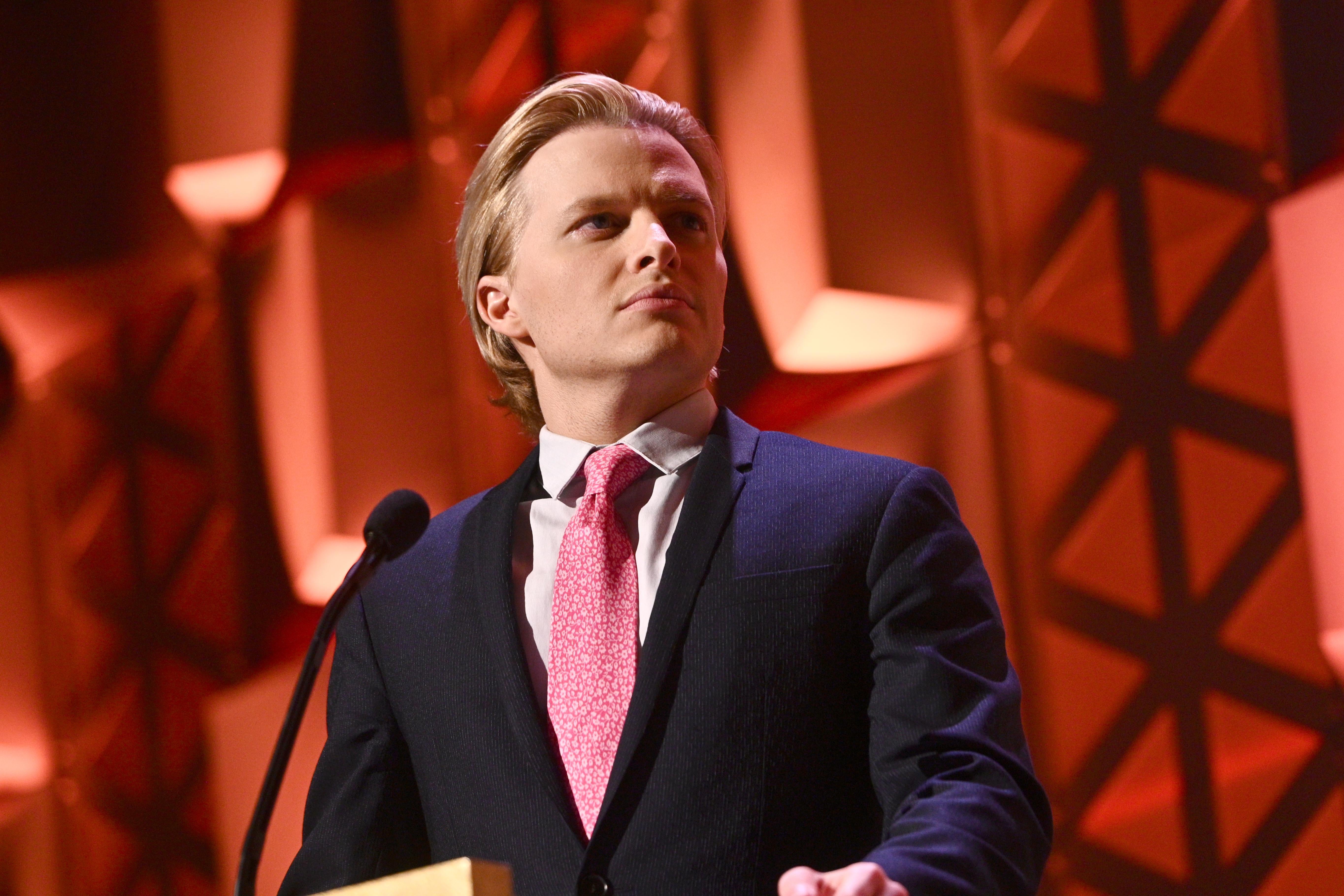 Ronan Farrow behind a podium with a red background.