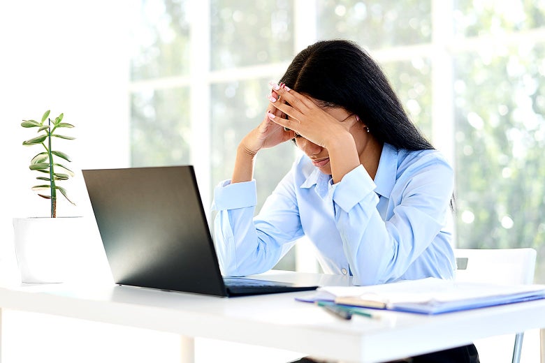 Young Black woman sitting in front of a laptop holding her head in her hands in frustration