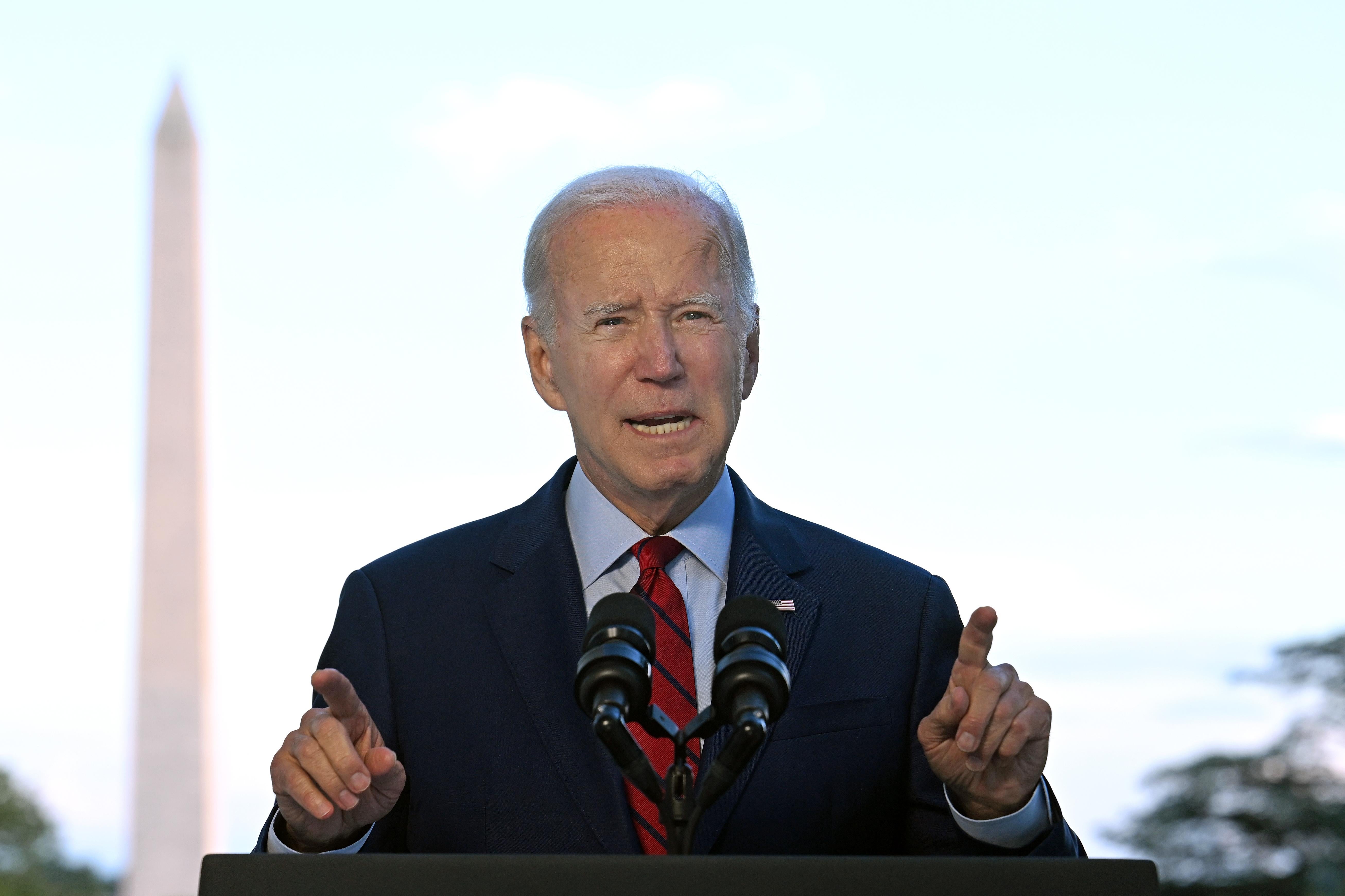 Biden points out with both of his fingers and the Washington Monument in the background.