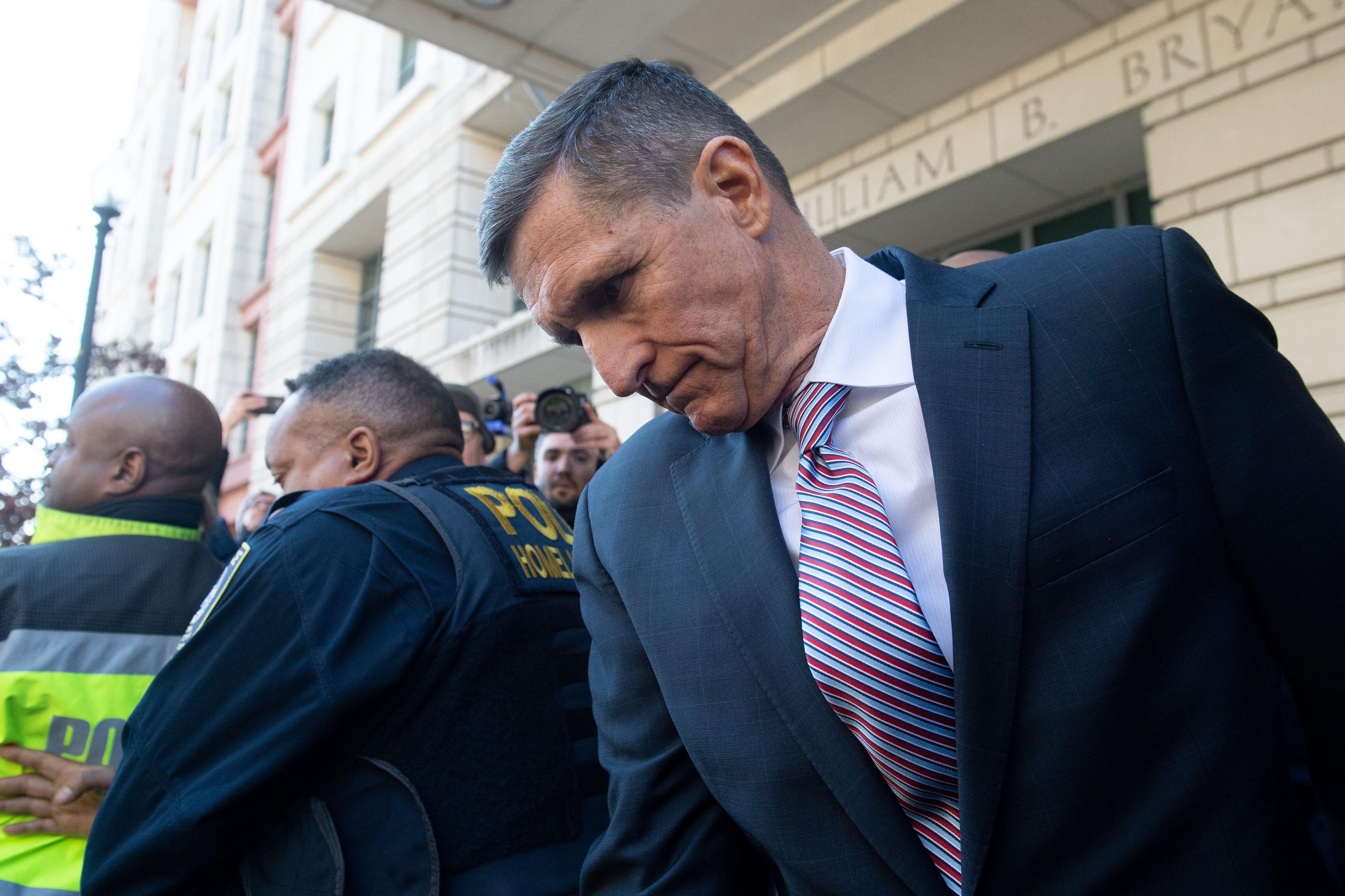 Michael Flynn looks down as he pushes through a crowd of reporters outside the court building.