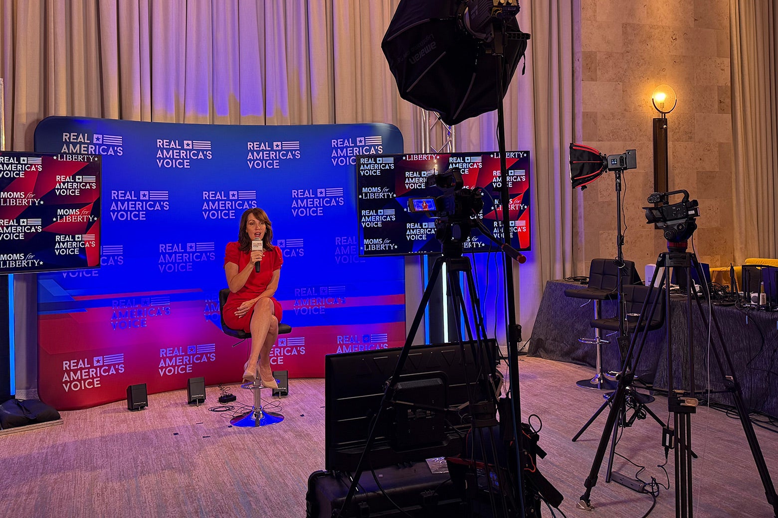 A show being filmed during the event; a woman is sitting on a stool onstage in front of the logo for Real America's Voice. 