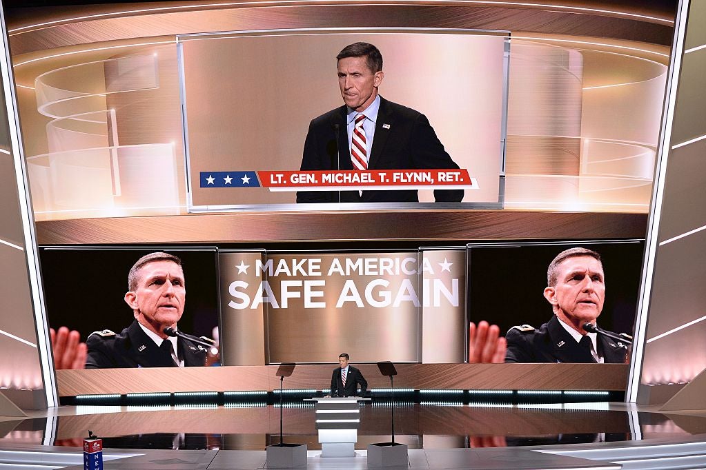 Flynn stands at a lectern as the words MAKE AMERICA SAFE AGAIN and several large images of his face are projected on the huge screen behind him.